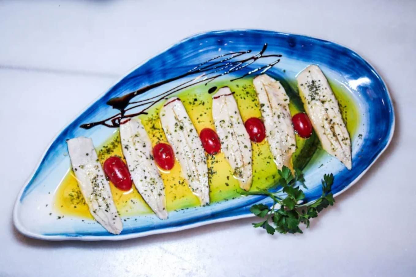 Plato de pescado en plato azul con tomates, rociado con aceite de oliva y glaseado balsámico.