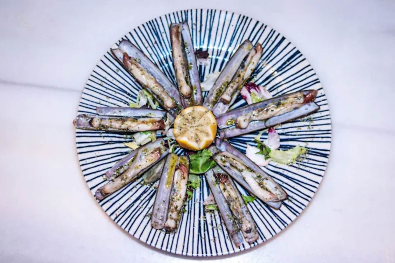 Navajas dispuestas en un plato decorativo con rodaja de limón y guarnición.