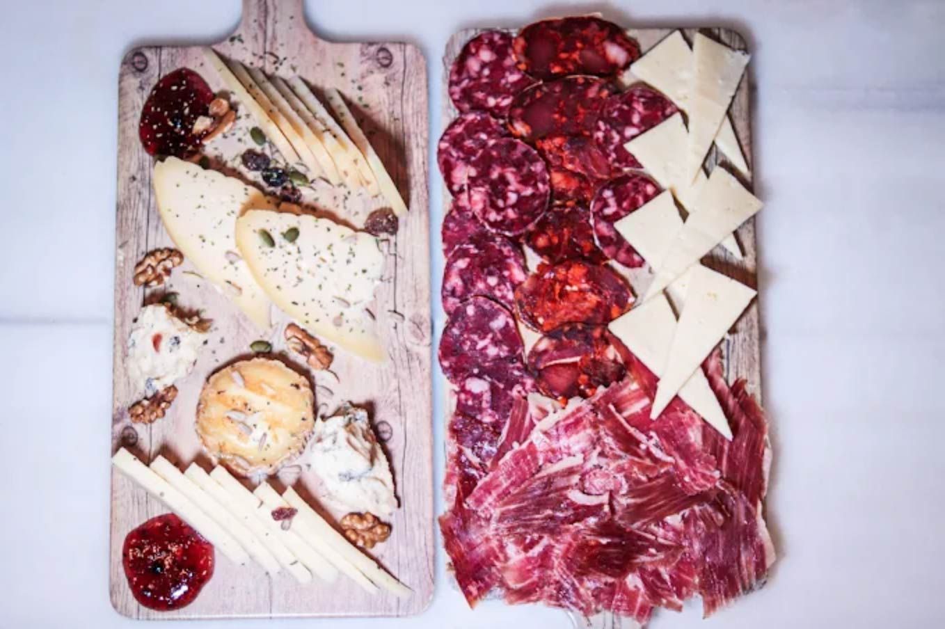 Tablas de embutidos con quesos, carnes, mermeladas y galletas en bandejas de madera.
