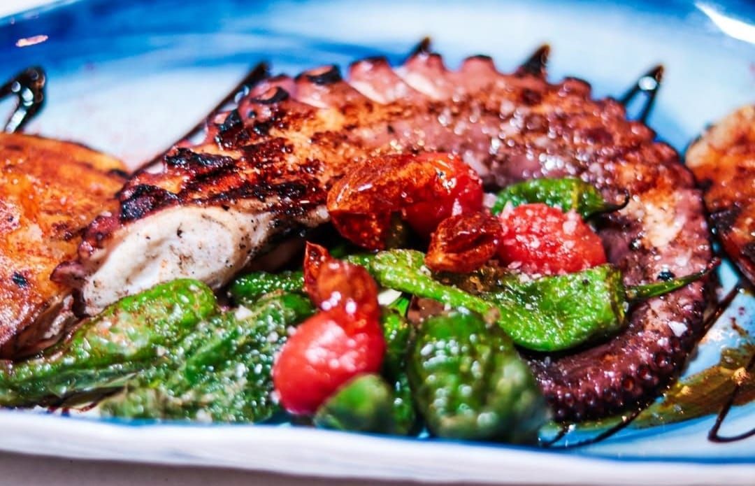 Pulpo a la plancha con pimientos y tomates en plato de borde azul.