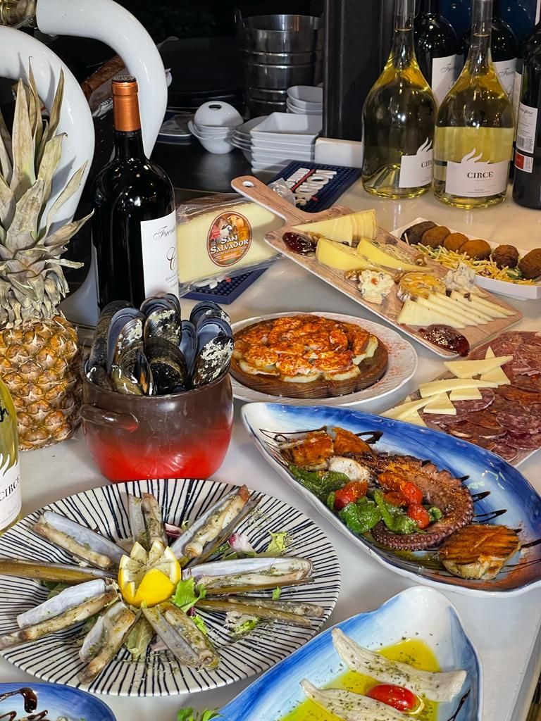 Una mesa repleta de diversos platos de mariscos, quesos y botellas de vino.
