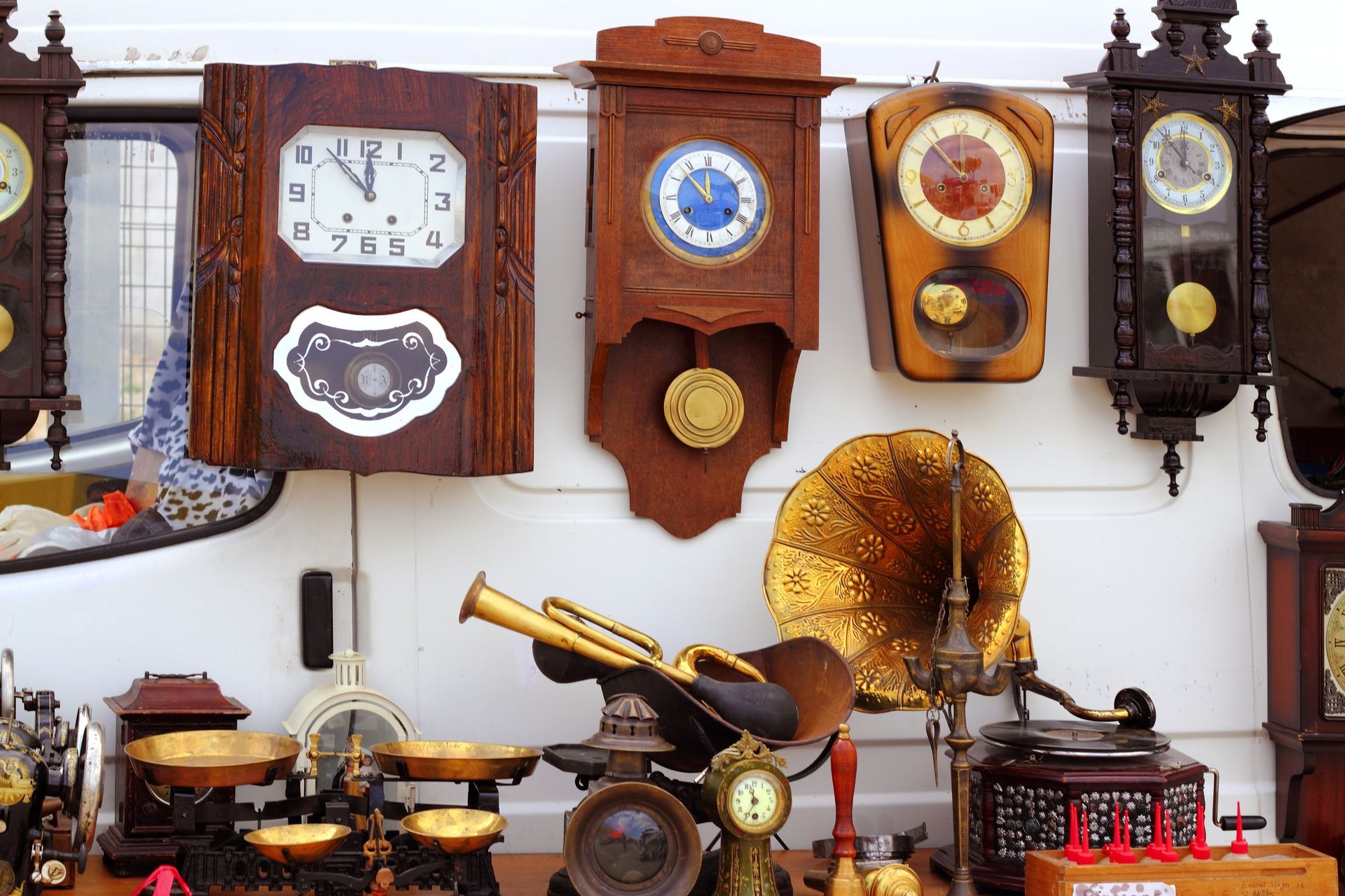 Des horloges murales anciennes et un phonographe en laiton sont exposés en vitrine.
