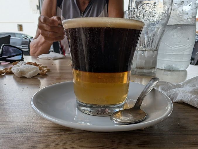 Un vaso de cerveza en un platillo con una cuchara sobre una mesa.