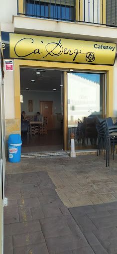 Un restaurante con un cartel amarillo y un bote de basura azul enfrente.