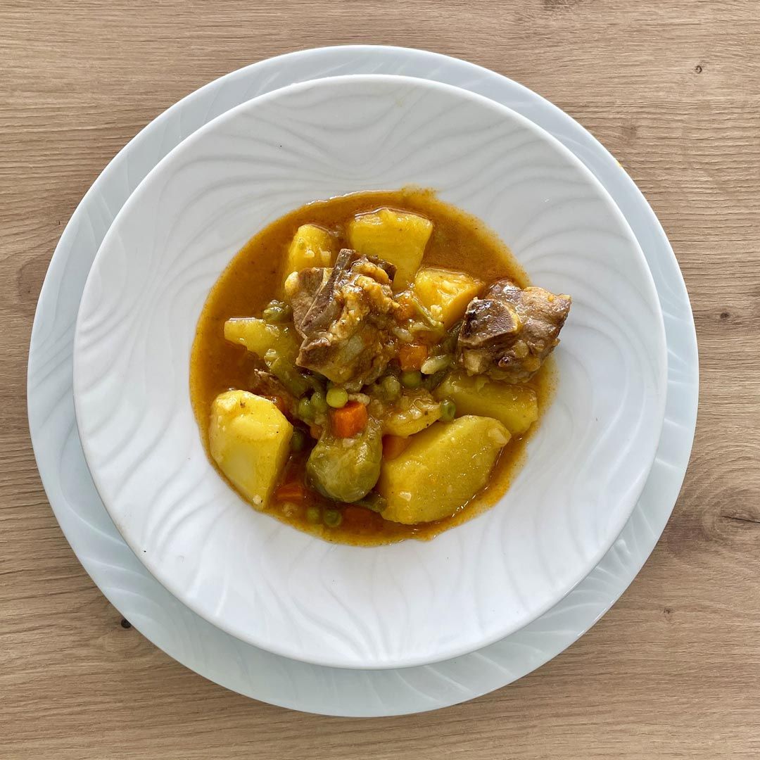 Guiso de carne y verduras en un recipiente blanco, sobre una mesa de madera.