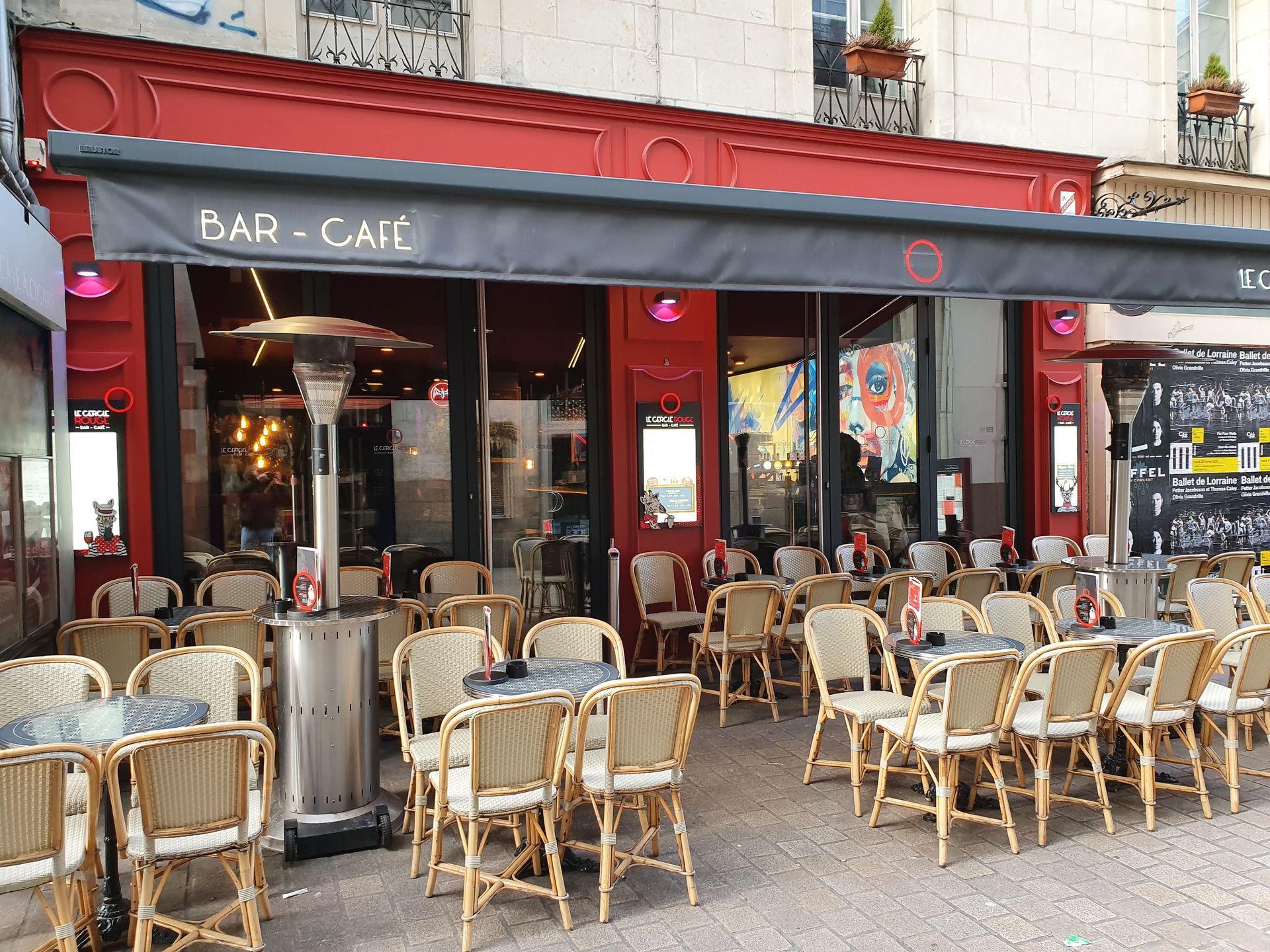 Terrasse extérieure d'un café à façade rouge avec auvent noir, tables et chaises.