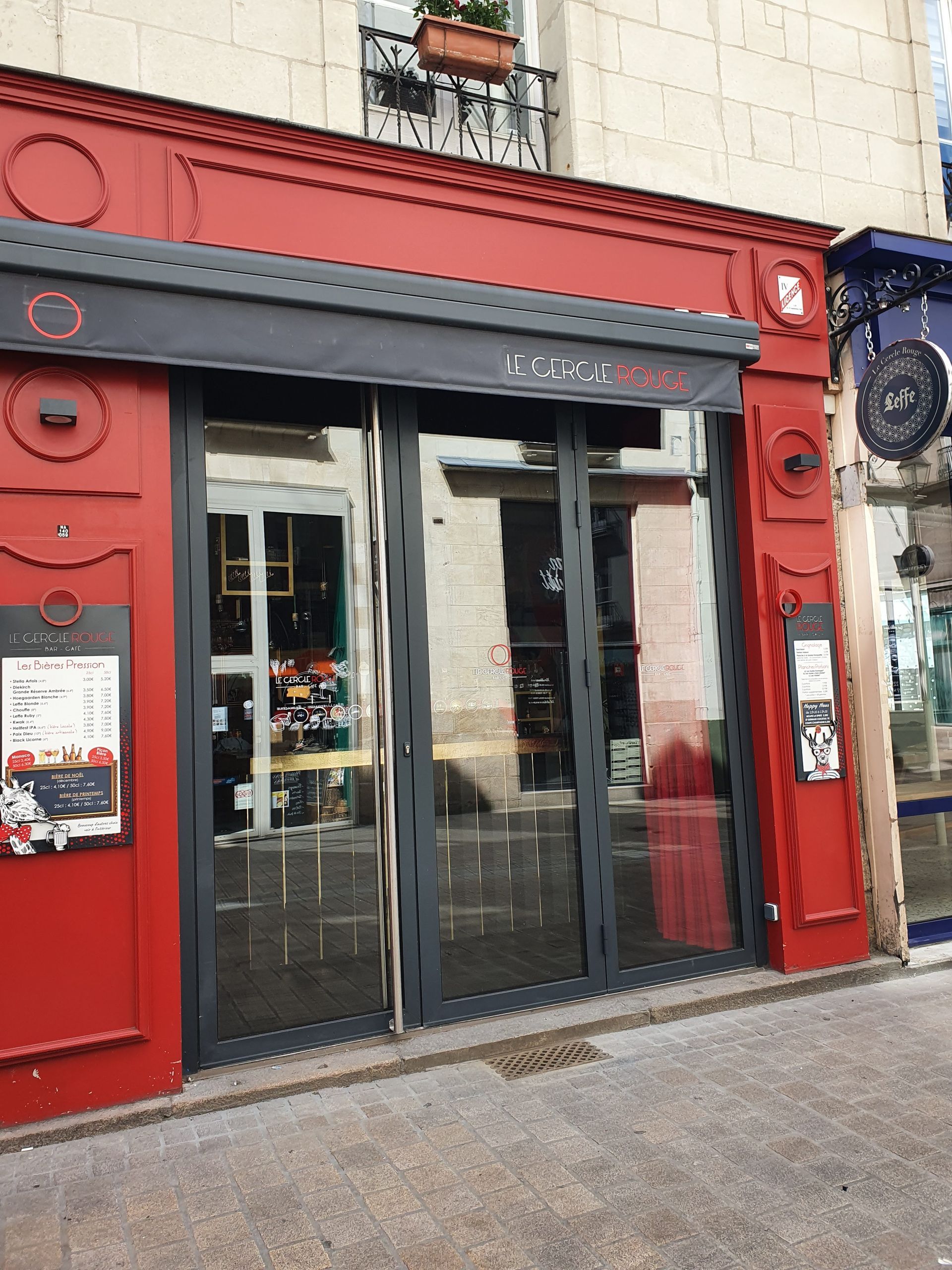 Façade rouge avec auvent foncé et portes vitrées.