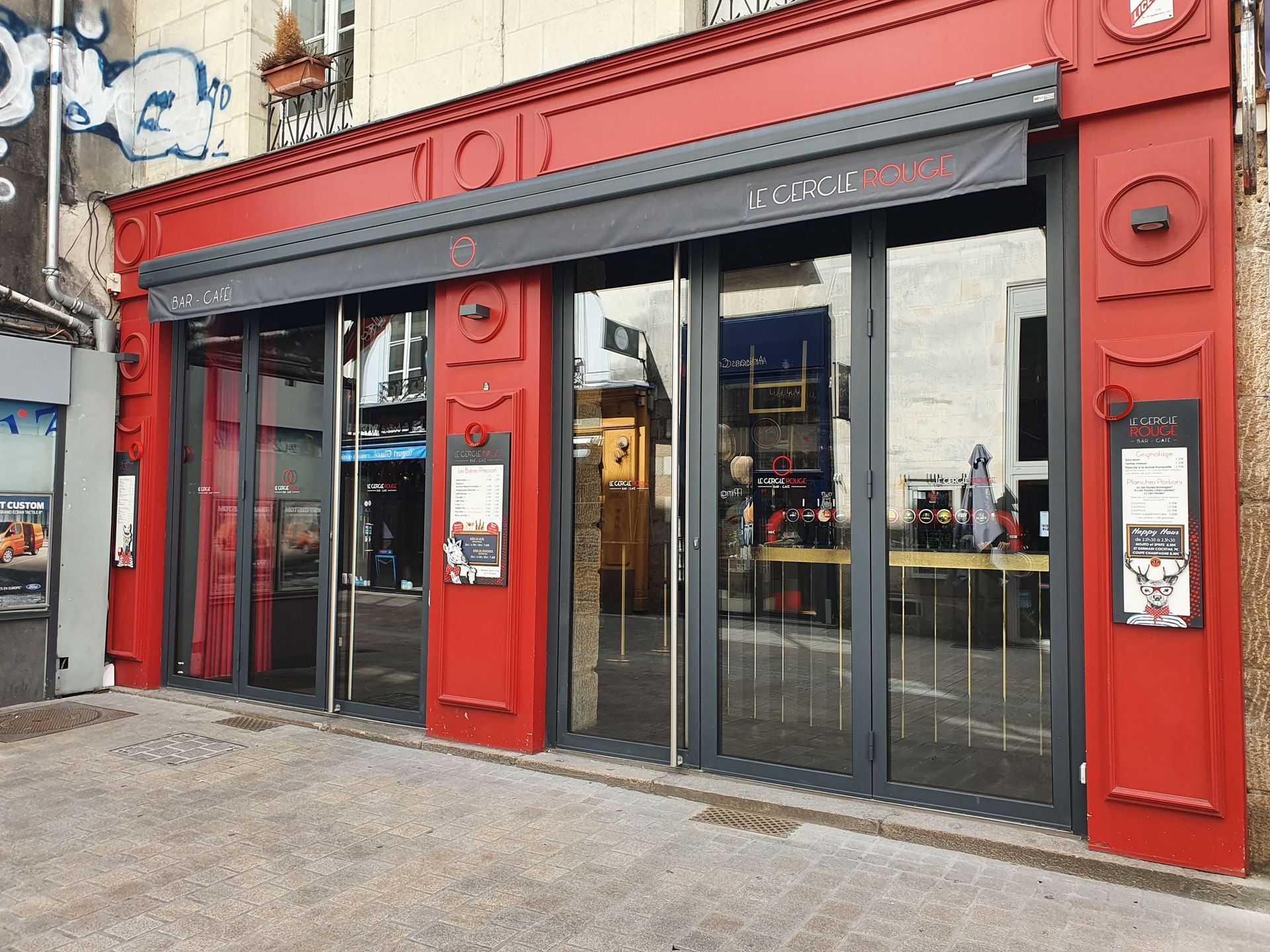 Boutique à encadrement rouge, portes vitrées et auvent noir.