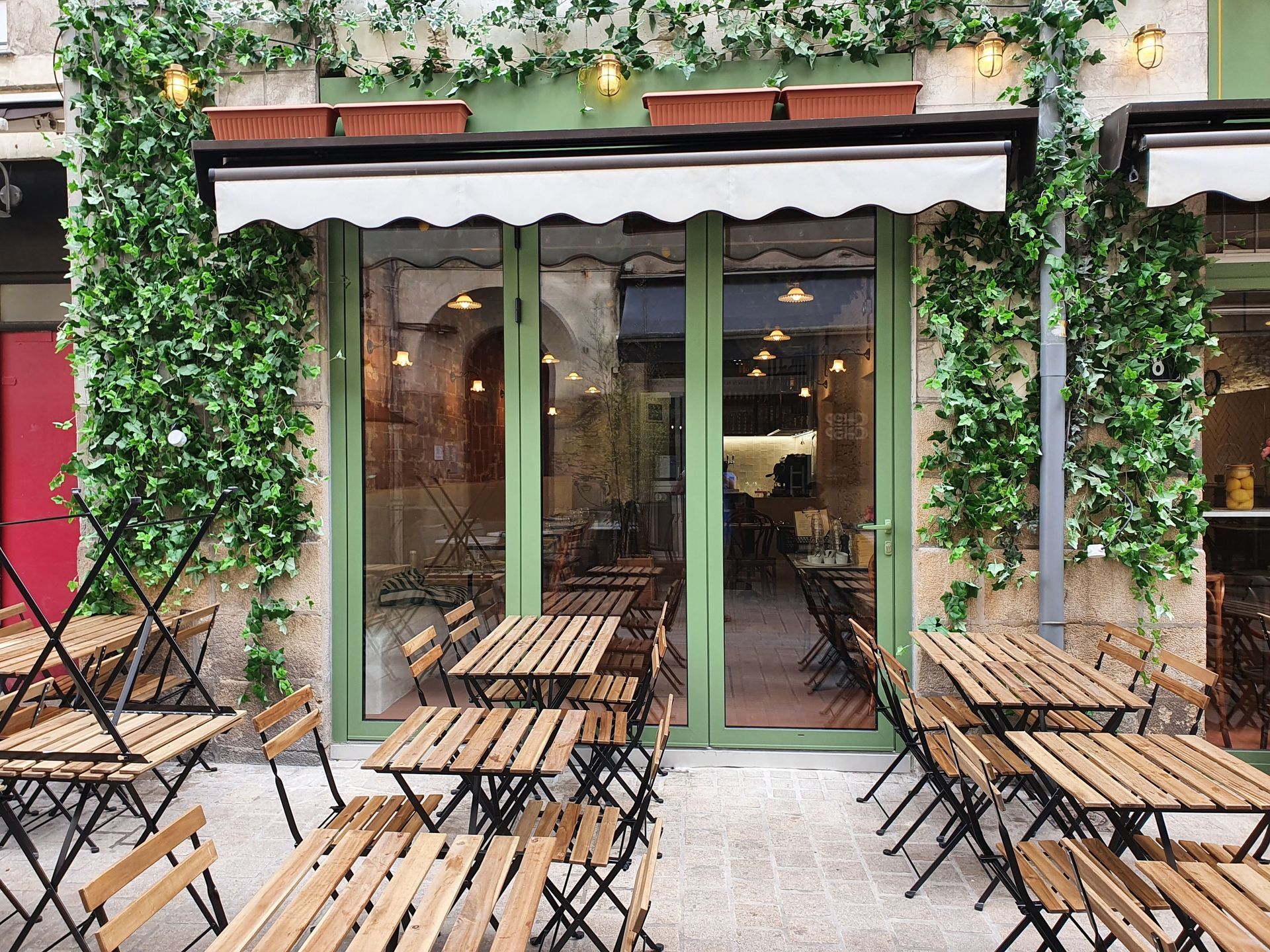Façade avec boiseries vertes, auvent et terrasse. Du lierre grimpe le long des murs.