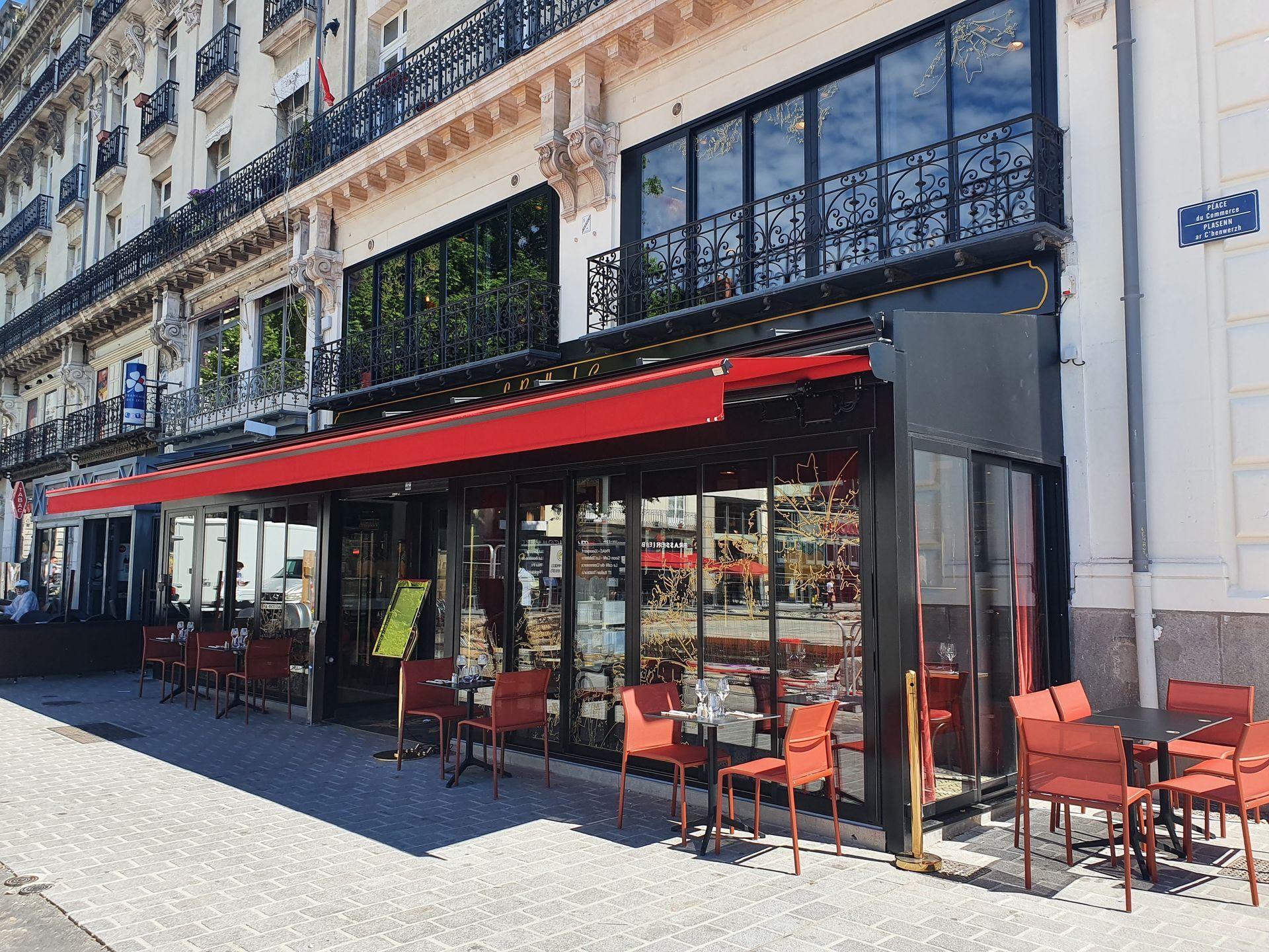 Un restaurant avec une terrasse couverte d'un auvent rouge, dans une rue de la ville.