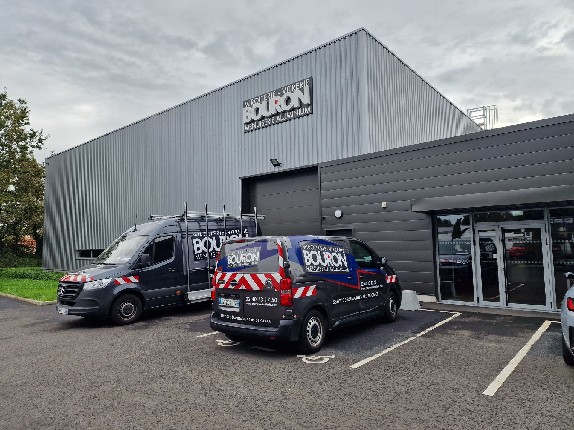 Bâtiment noir et gris avec des camionnettes garées devant.