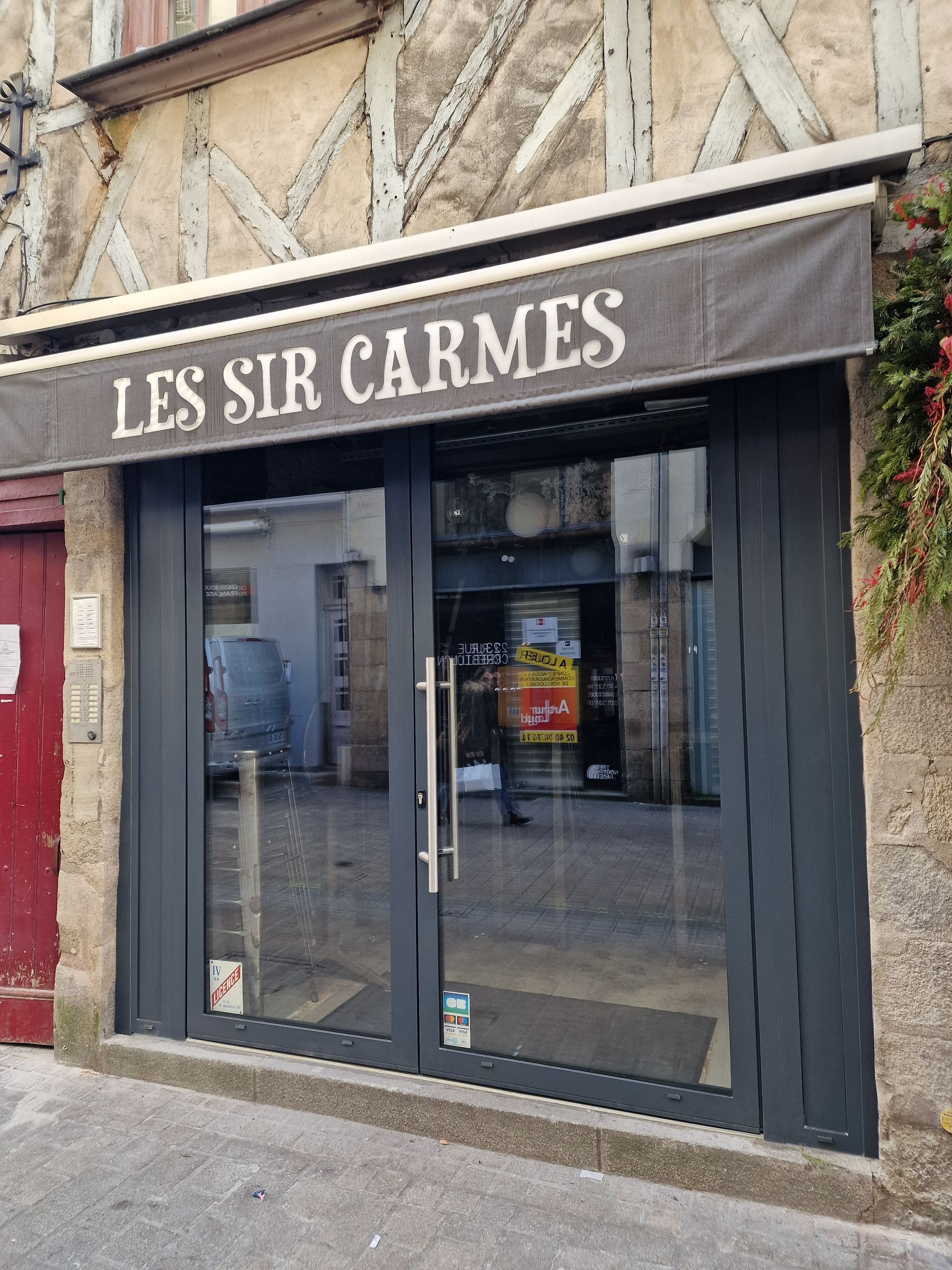Entrée de la boutique Les Sir Carmes avec portes vitrées, auvent et texte.
