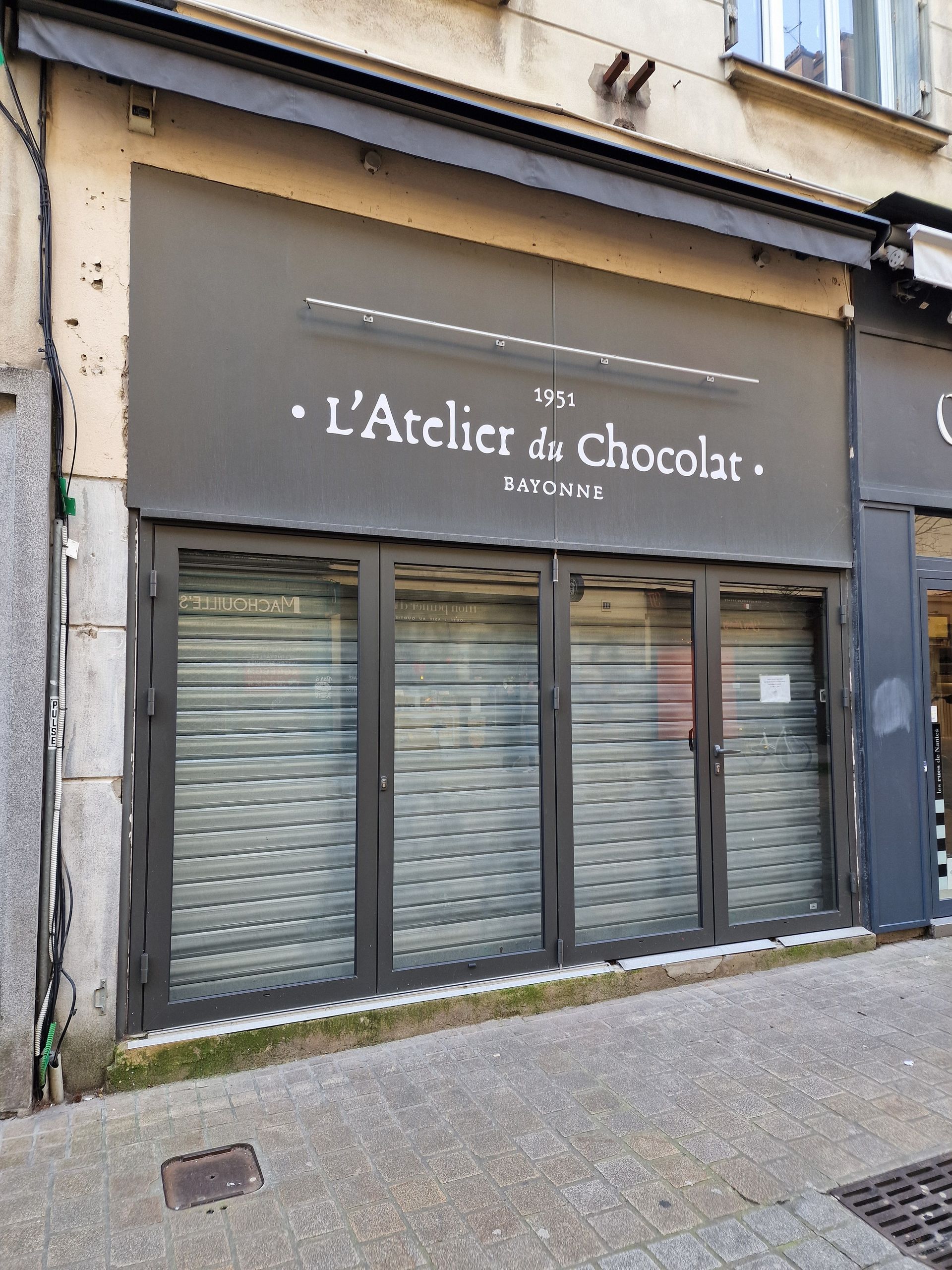 Façade de magasin portant l'inscription L'Atelier du chocolat sur une façade gris foncé.