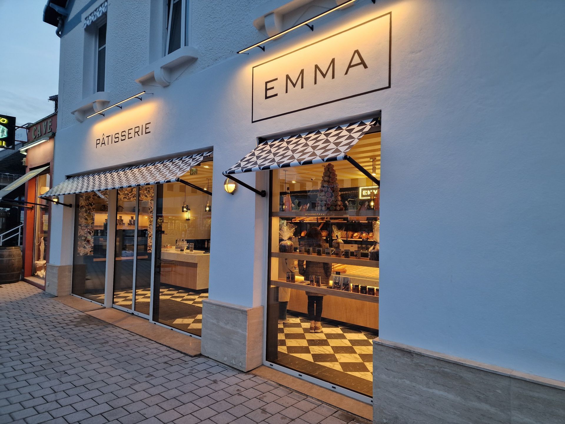 Façade de la pâtisserie Emma avec auvent, éclairage et enseigne, présentant des produits.