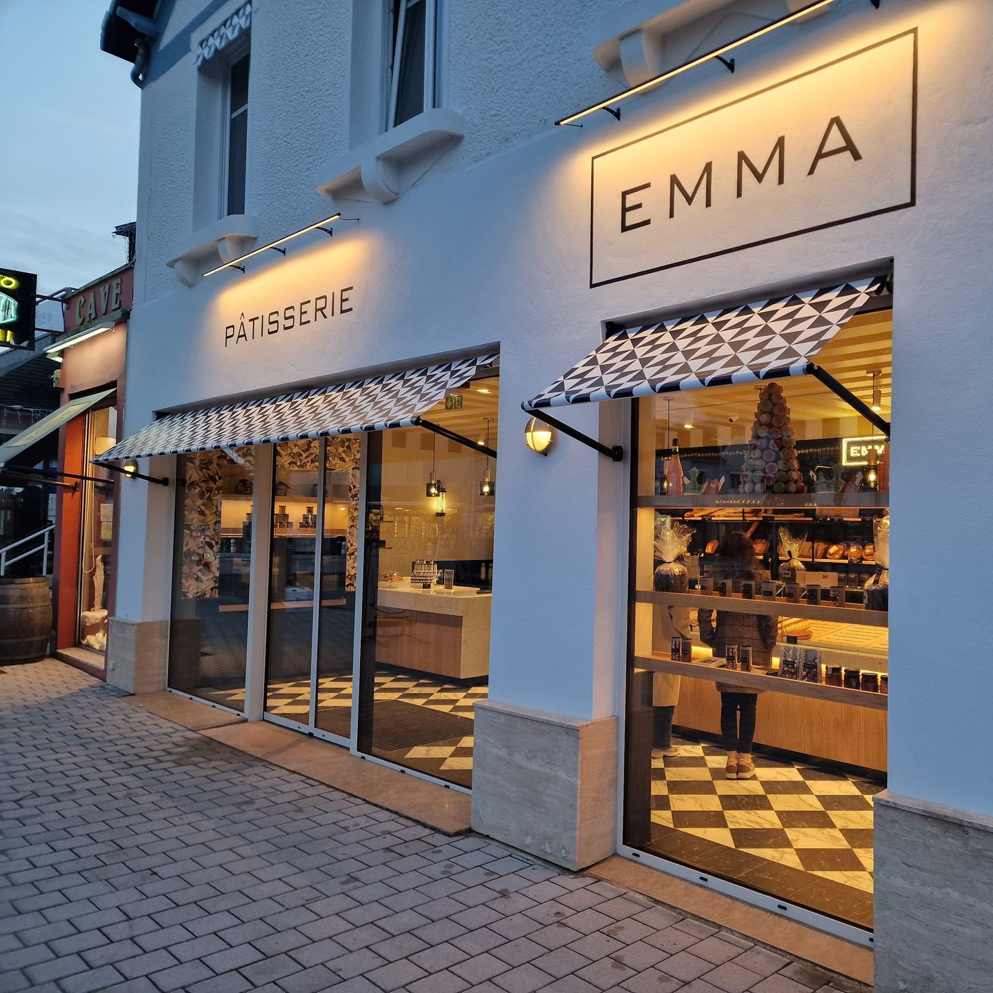 Extérieur d'une pâtisserie avec des auvents, des vitrines et un sol à damier.