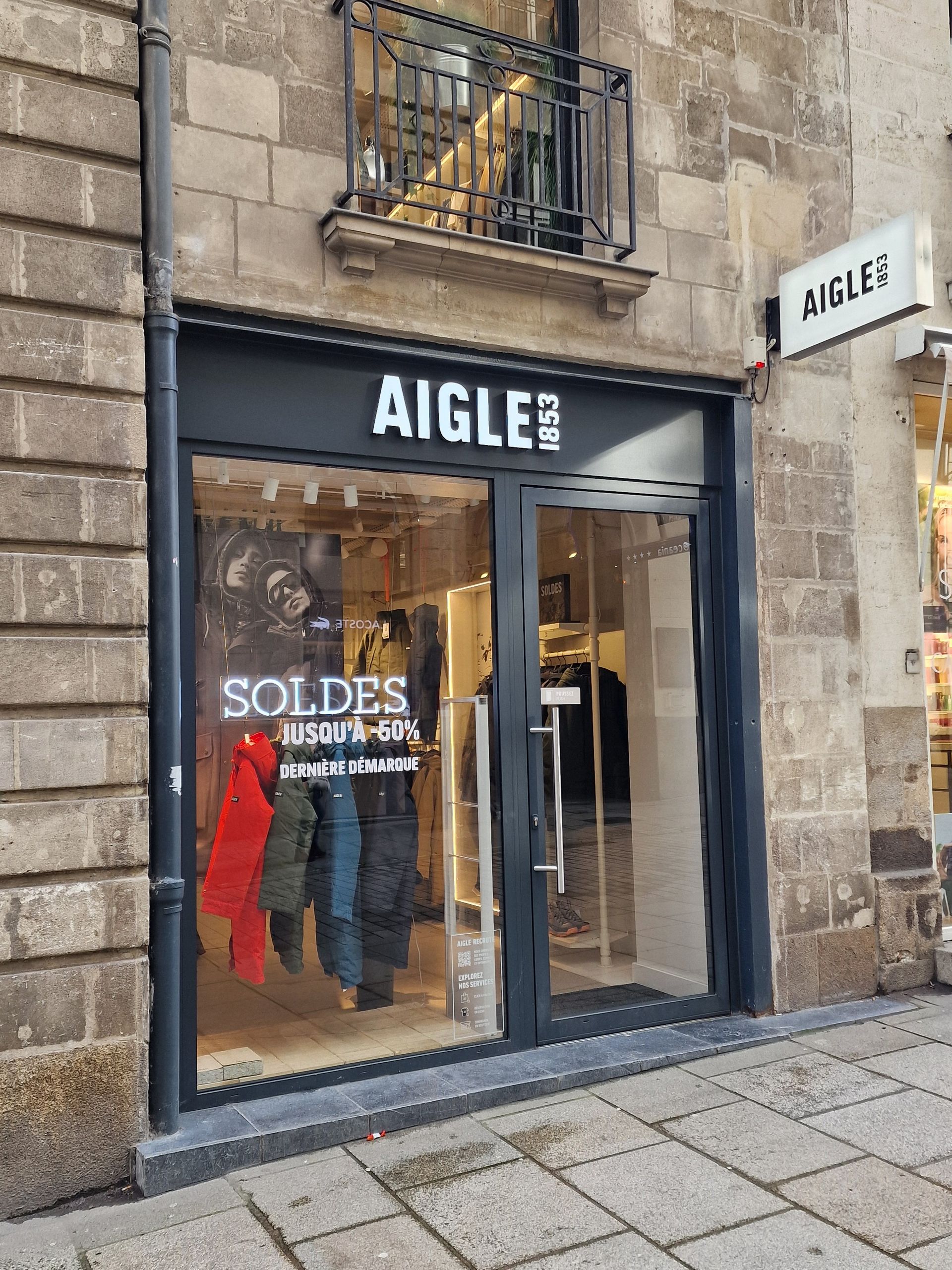 Entrée du magasin AIGLE, porte vitrée, façade en pierre.