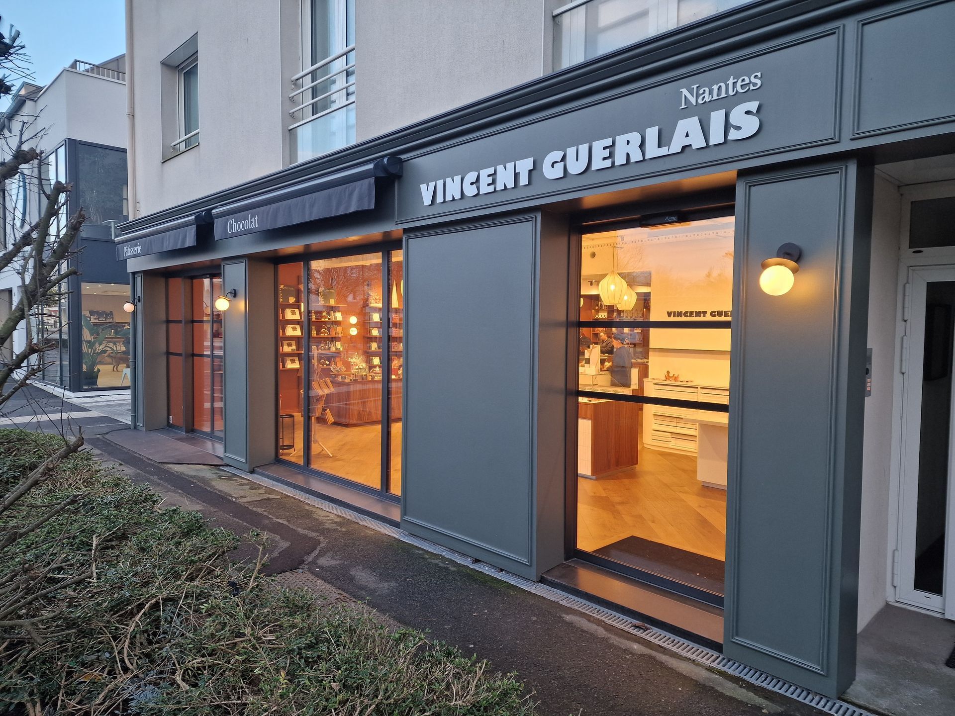 Extérieur d'une boutique avec des vitrines et un auvent sombre, éclairé de l'intérieur.