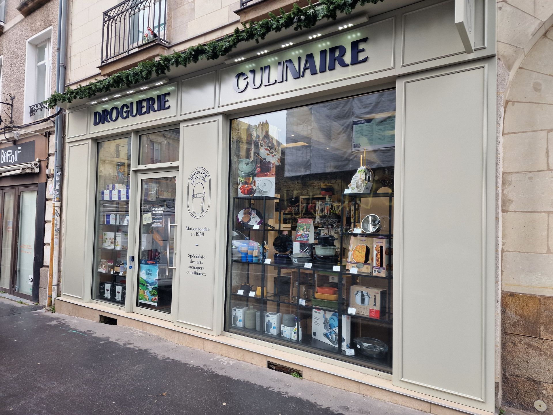 Une devanture de magasin avec une enseigne DROGUERIE CULINAIRE, exposant des produits culinaires en vitrine.