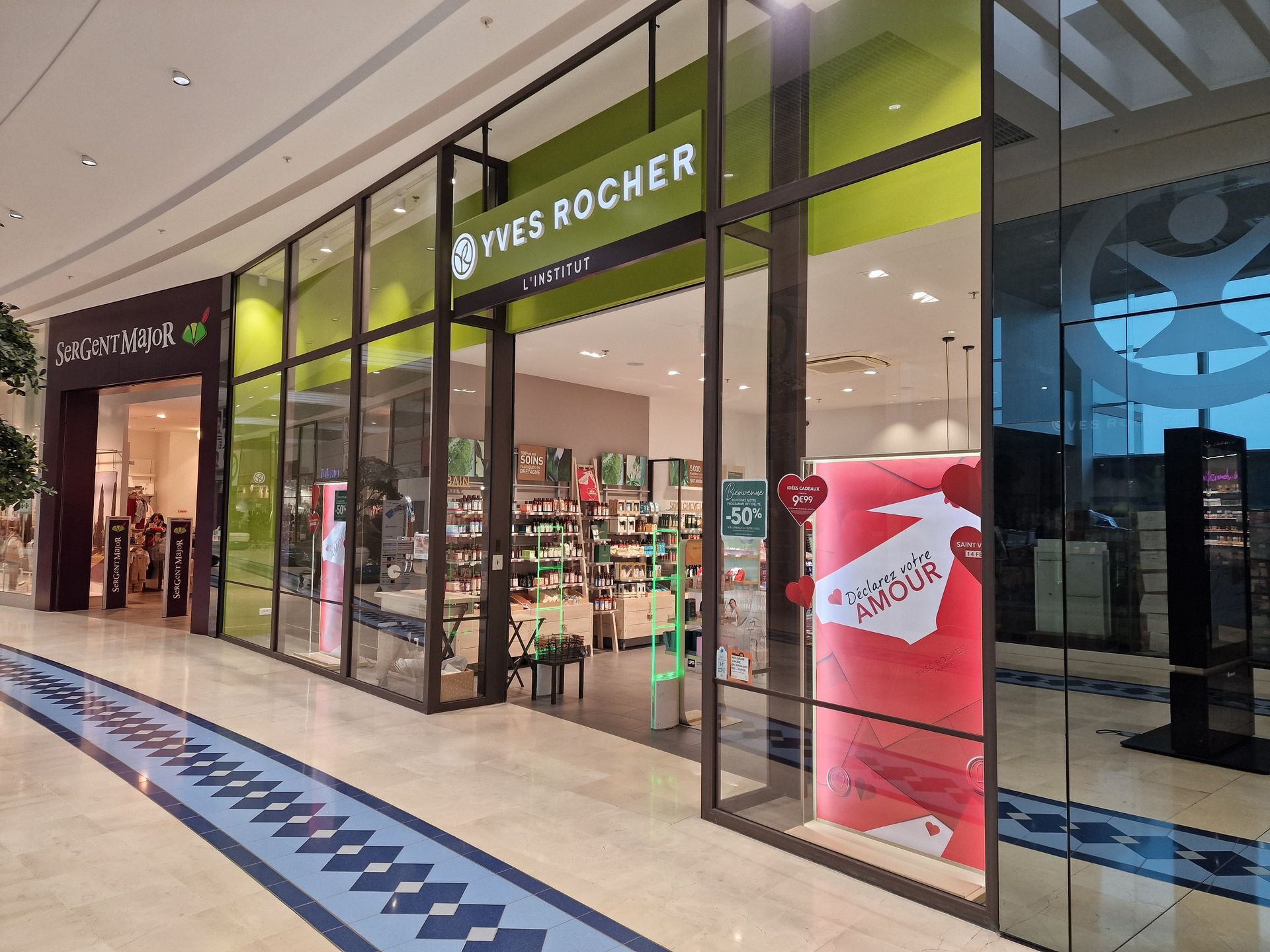 Entrée d'une boutique dans un centre commercial, avec une identité visuelle verte et blanche.