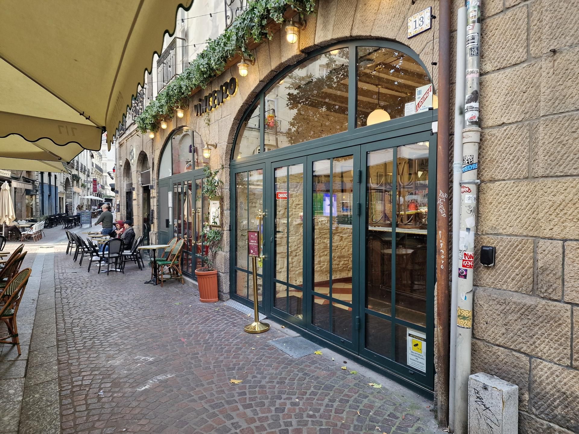 Façade de café avec entrée voûtée et terrasse donnant sur une rue pavée.