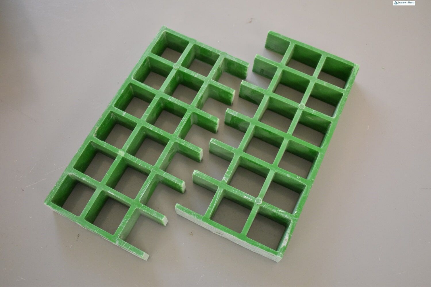 Grade de plástico verde, quebrada em duas partes, sobre uma superfície cinza clara.