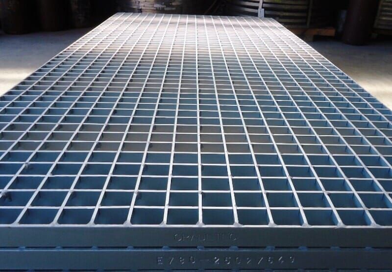 Grade metálica, provavelmente de aço, com padrão de grade quadrada, empilhada em um armazém ou ambiente similar.