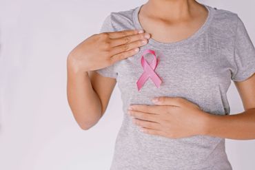 Eine Frau mit einer rosa Schleife, die ihre Brust berührt, symbolisiert durch das Bewusstsein für Brustkrebs.