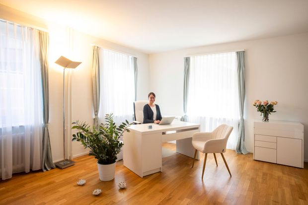 Zimmer mit medizinischer Ausrüstung und einer Behandlungsliege. Weisse und grüne Wände, Holzboden und Fenster.