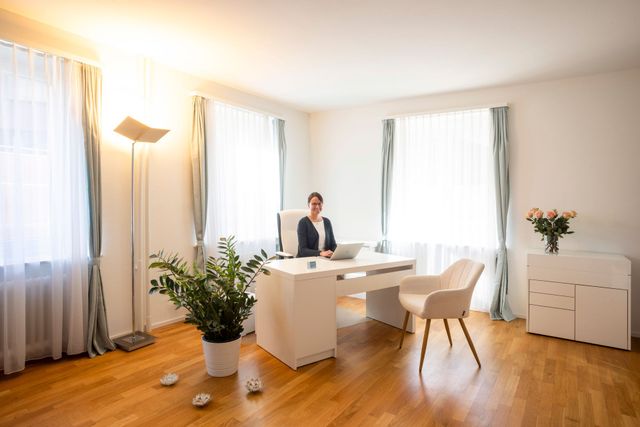 Zimmer mit medizinischer Ausrüstung und einer Behandlungsliege. Weisse und grüne Wände, Holzboden und Fenster.