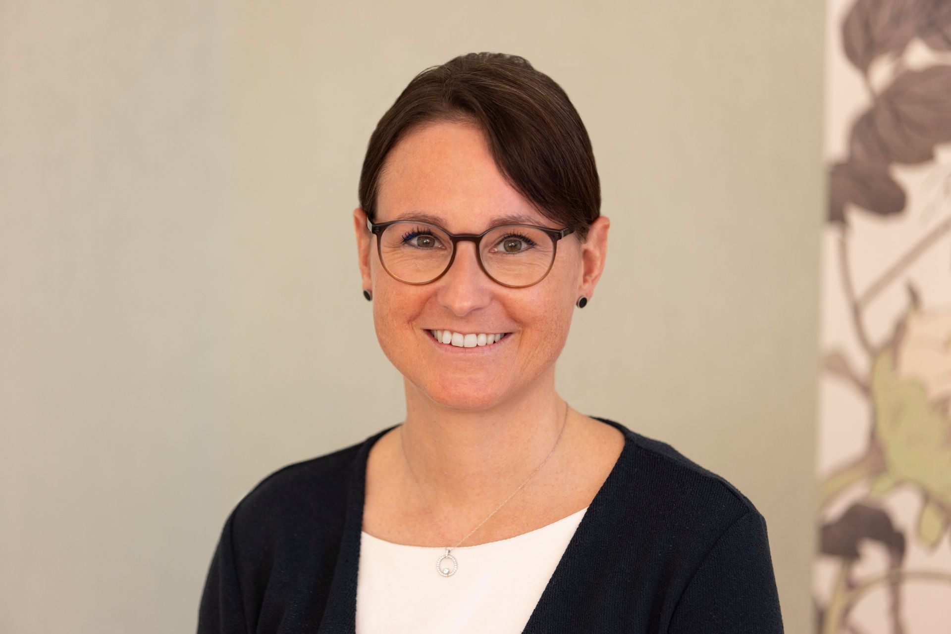 Eine Frau mit Brille lächelt in die Kamera; sie trägt ein gestreiftes Hemd und eine Perlenkette.