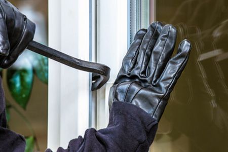 Ein Einbrecher schlägt mit einem Schraubenschlüssel ein Fenster ein.