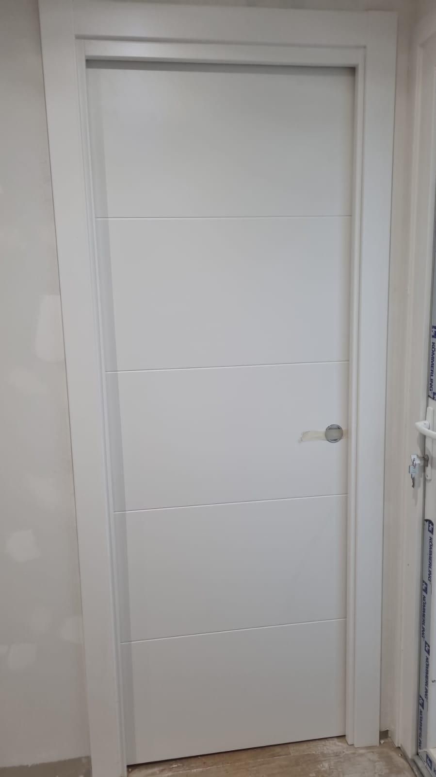 Puerta interior de color blanco con lineas horizontales, enmarcada en blanco, tirador metálico.