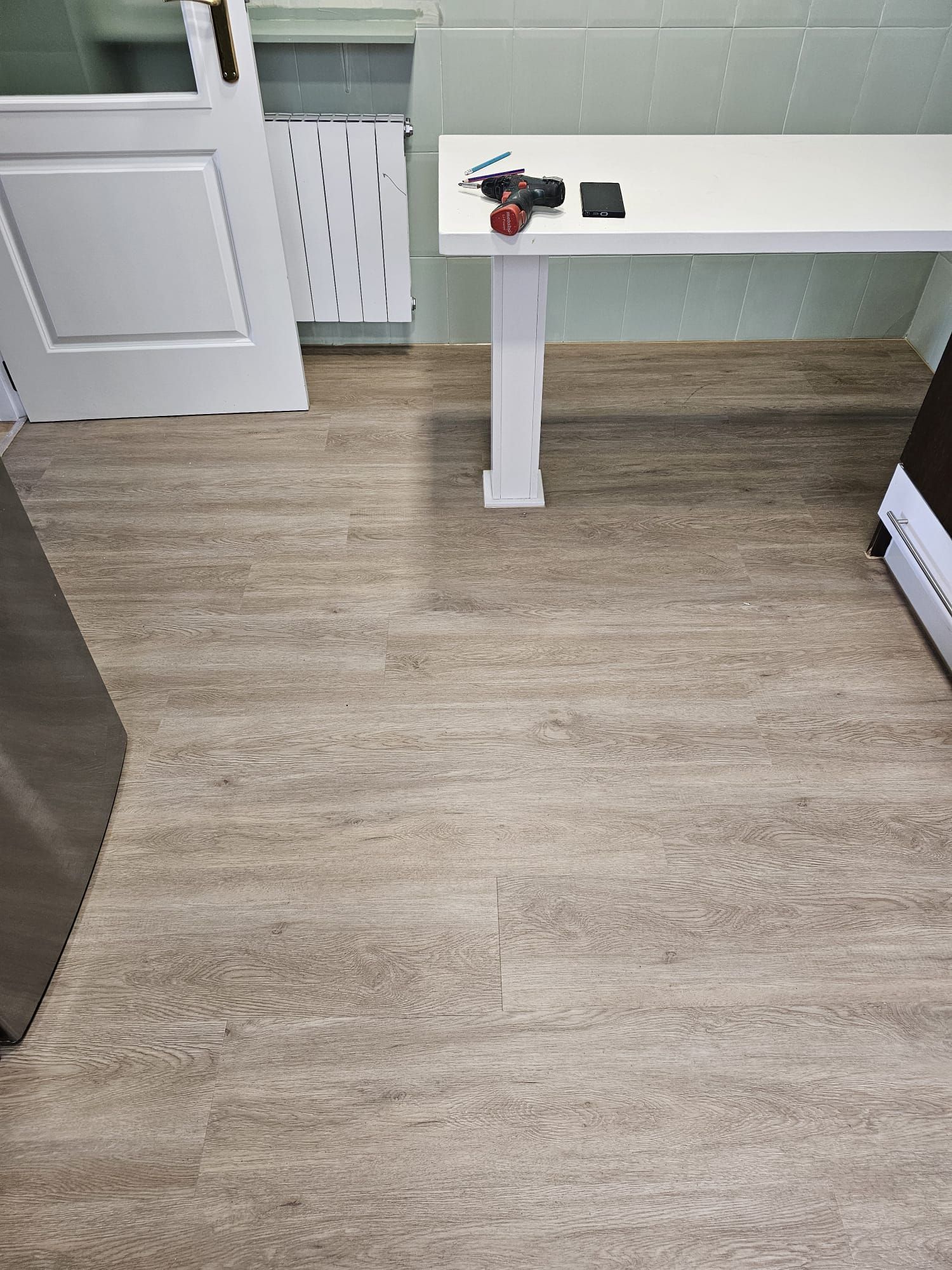 Suelo de aspecto madera clara con una mesa blanca y puerta cerrada en una habitación.