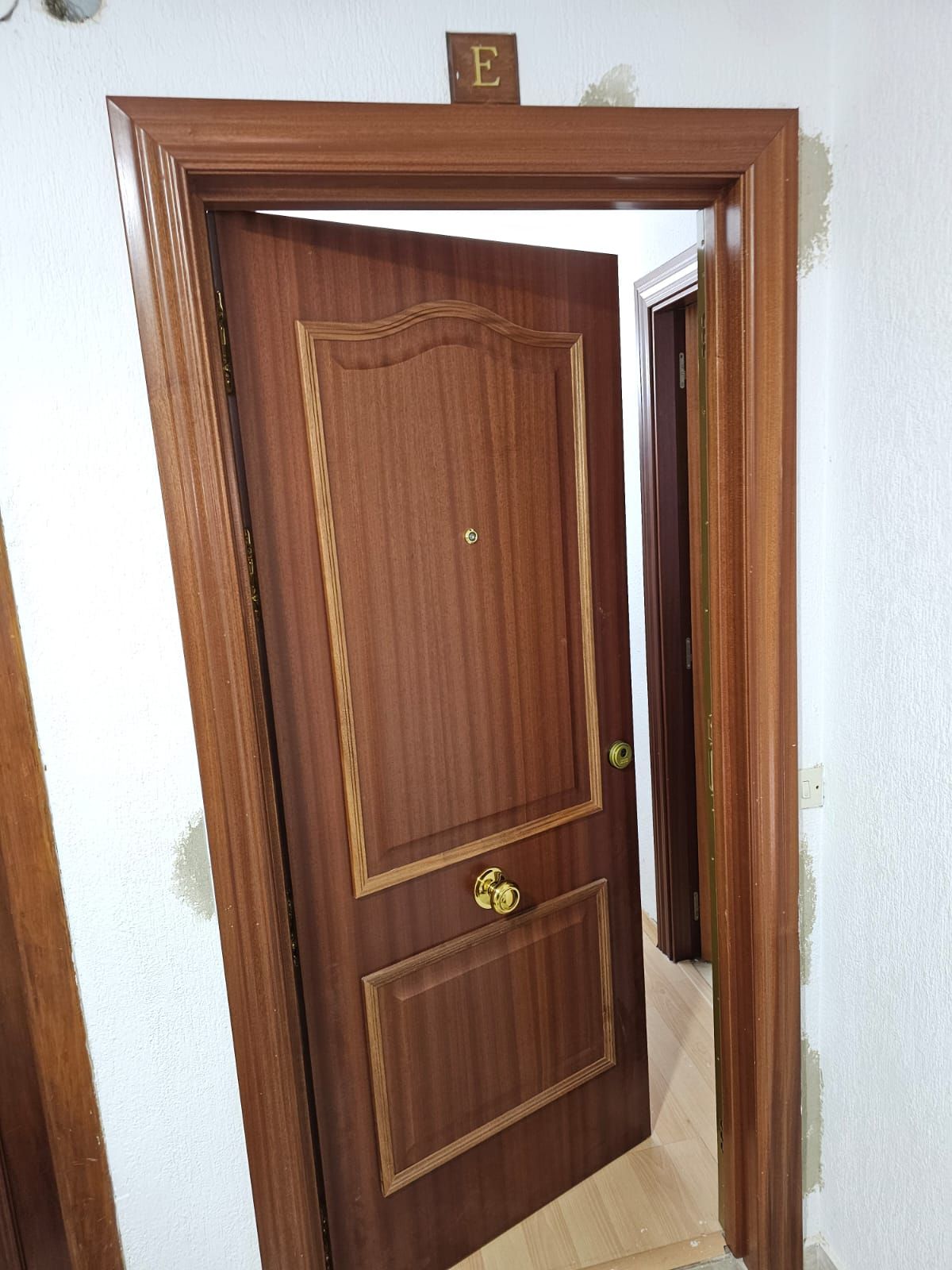 Puerta de madera entreabierta, marco con la letra 