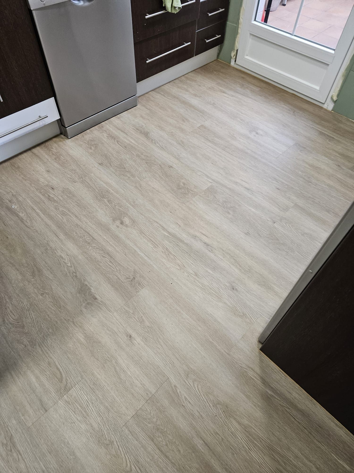 Piso con diseño de vetas de madera clara en una cocina, con lavavajillas y gabinetes oscuros visibles.