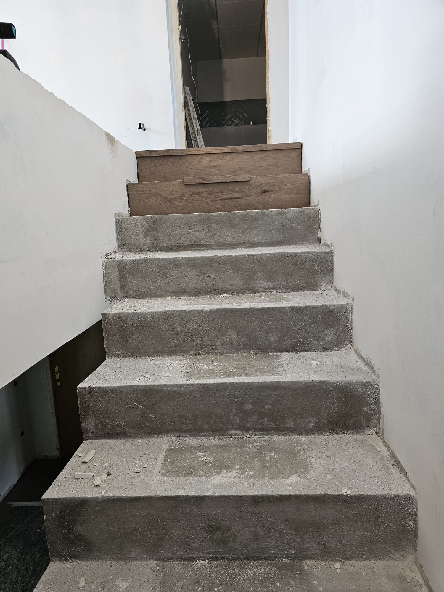 Escalera de hormigón que sube con un escalón de madera en la parte superior. Paredes blancas.