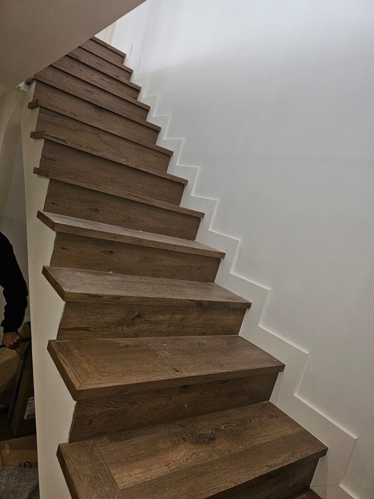 Escalera de madera con contrahuellas blancas que asciende contra una pared blanca.