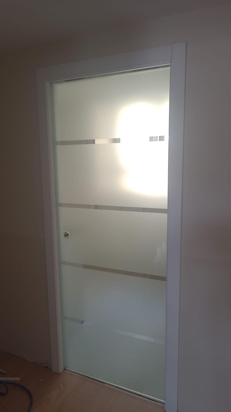 Puerta de vidrio esmerilado con rayas horizontales, enmarcada en blanco. La luz del sol se filtra a través de ella.