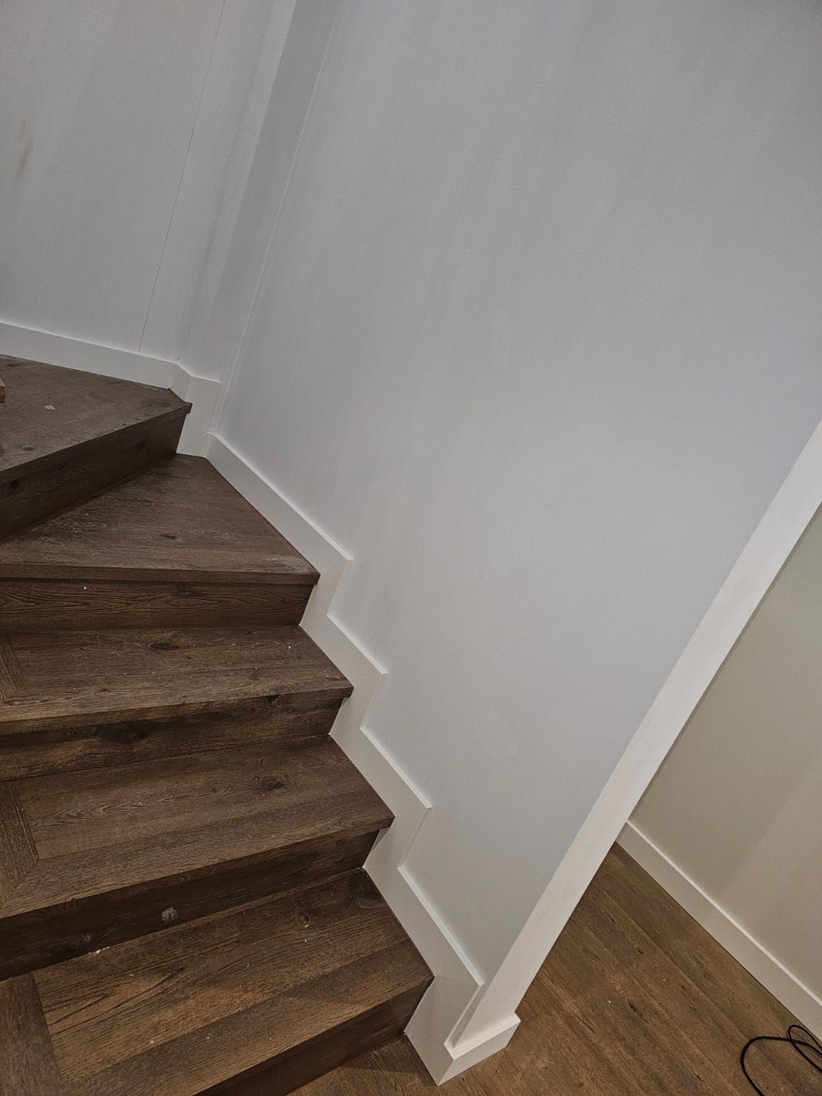 Escalera de madera con paredes y molduras blancas.