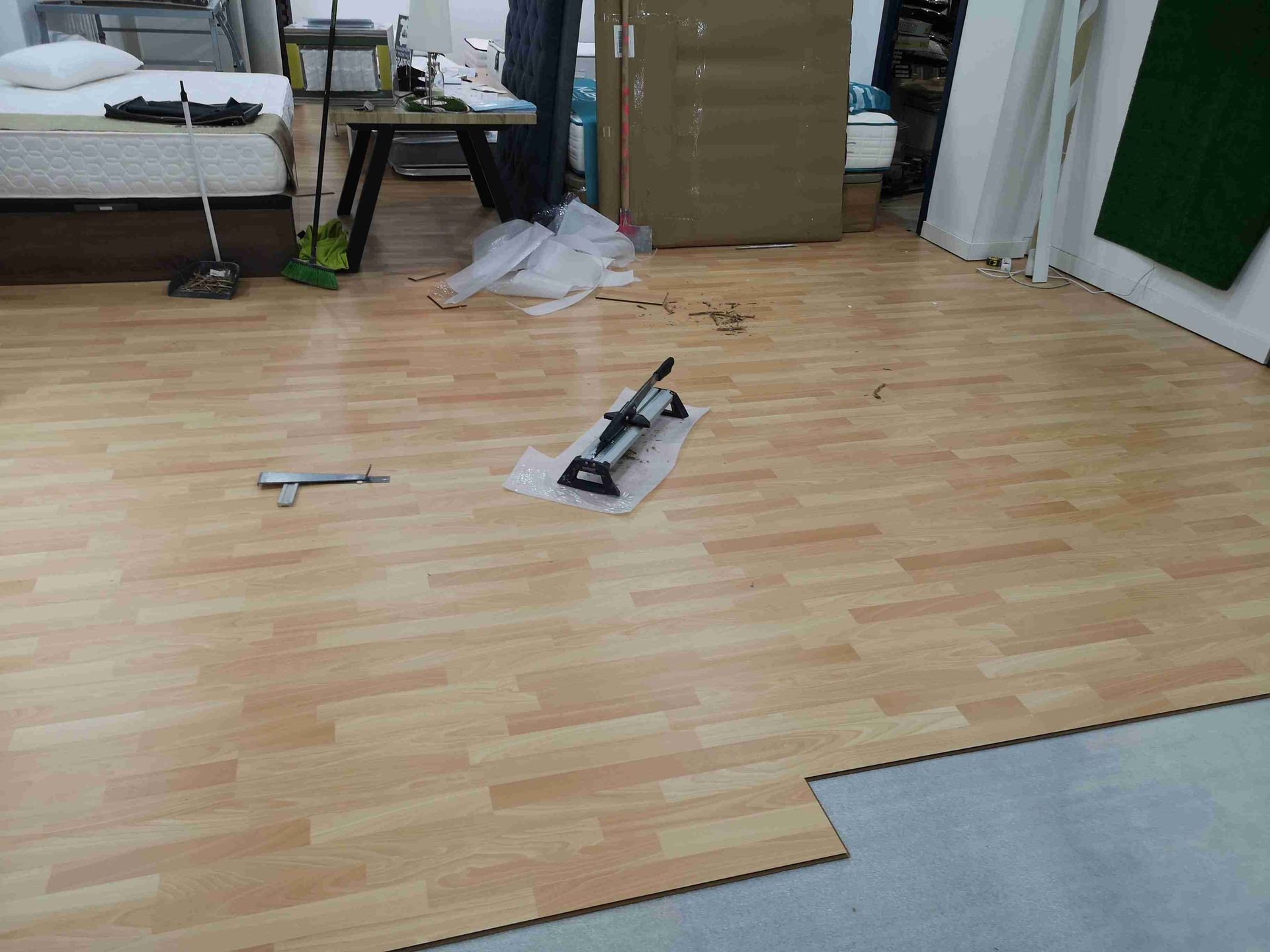 Instalación de suelo laminado con aspecto de madera en una habitación. Hay una cortadora y herramientas en el suelo.