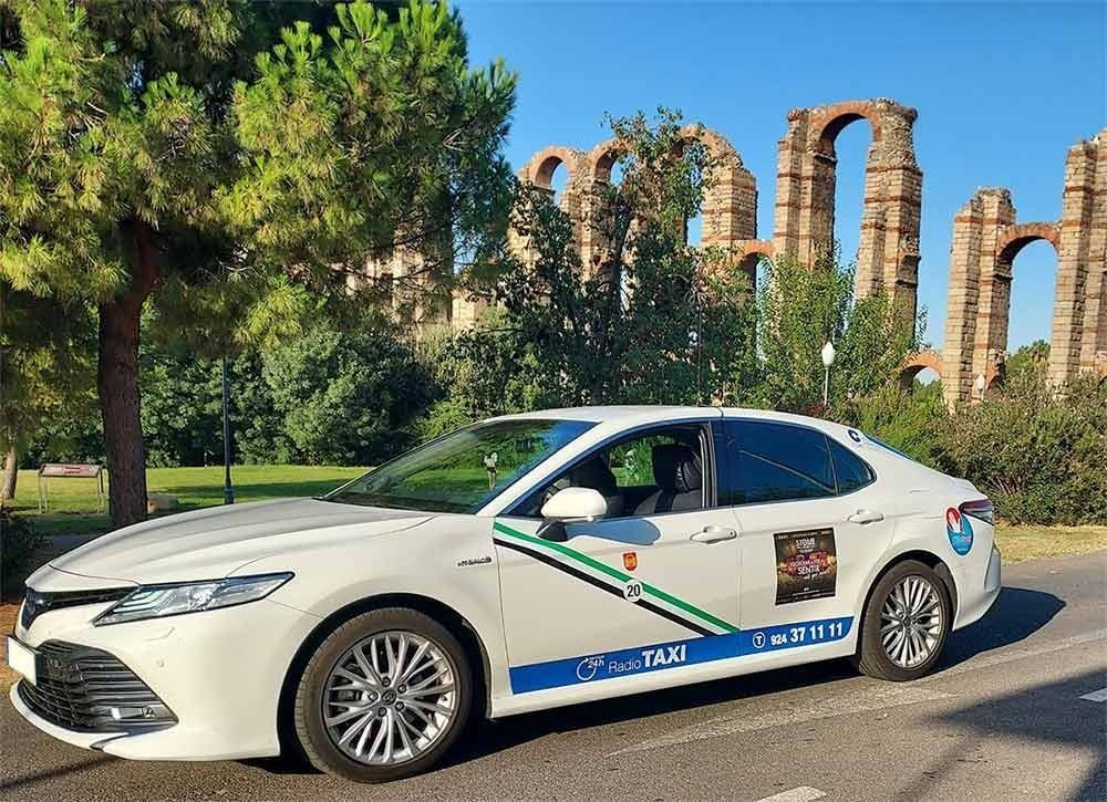 Un coche blanco está estacionado al costado de la carretera frente a un edificio en ruinas.