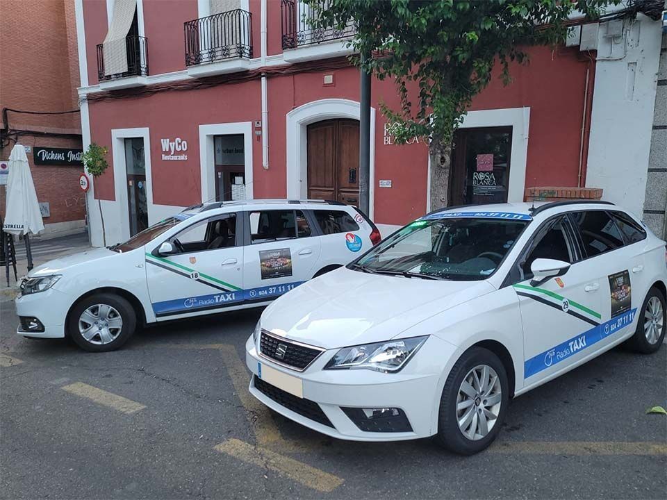 Dos coches blancos están aparcados delante de un edificio rojo.