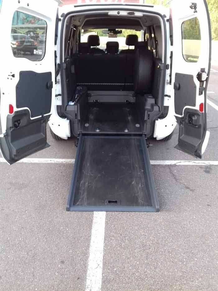 Una camioneta blanca con una rampa en la parte trasera está estacionada en un estacionamiento.