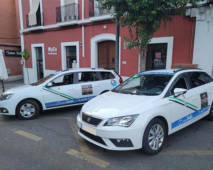 Dos coches blancos están aparcados delante de un edificio rojo.