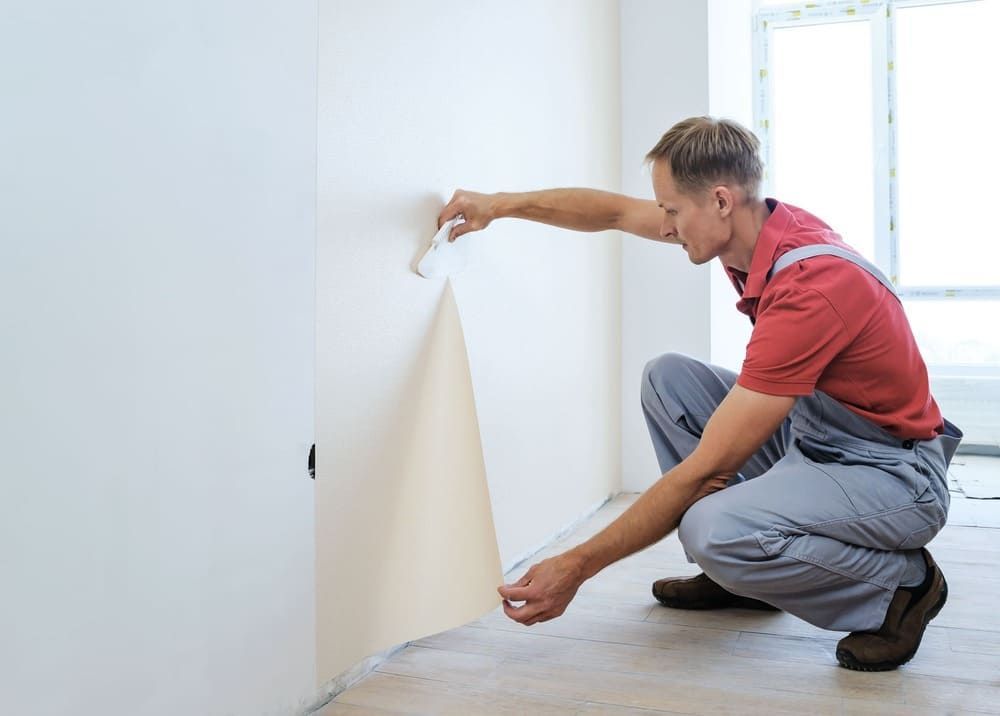 Ein Mann kniet nieder, um Tapeten von einer Wand zu entfernen.