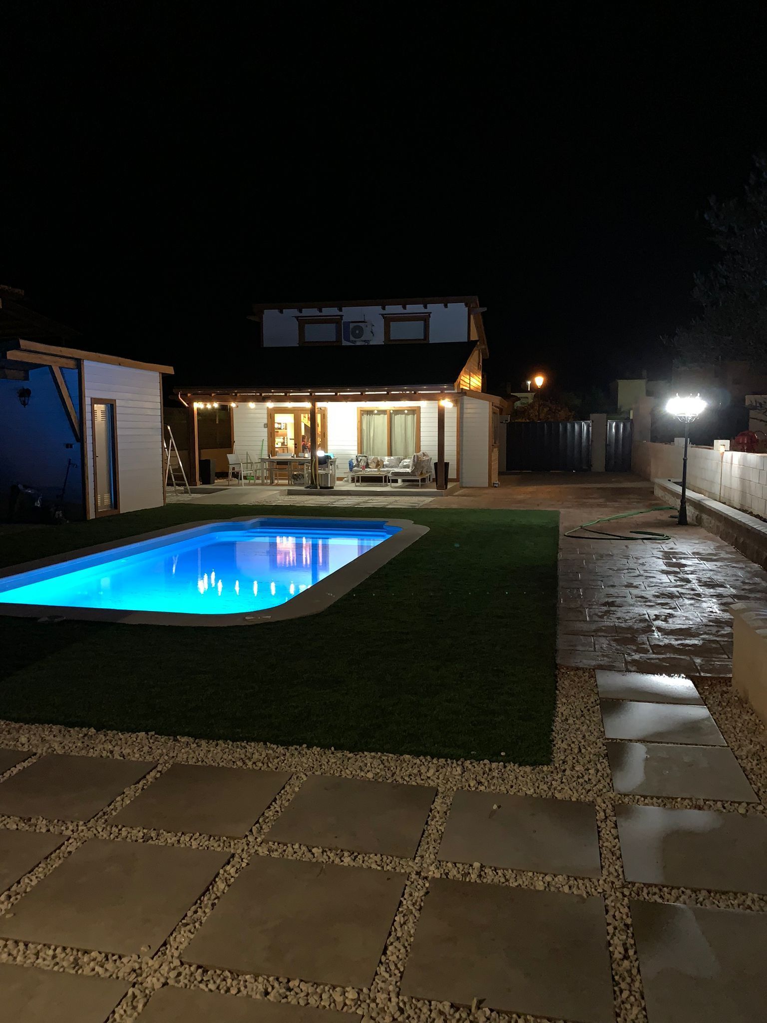 Una gran piscina está en el patio trasero de una casa por la noche.