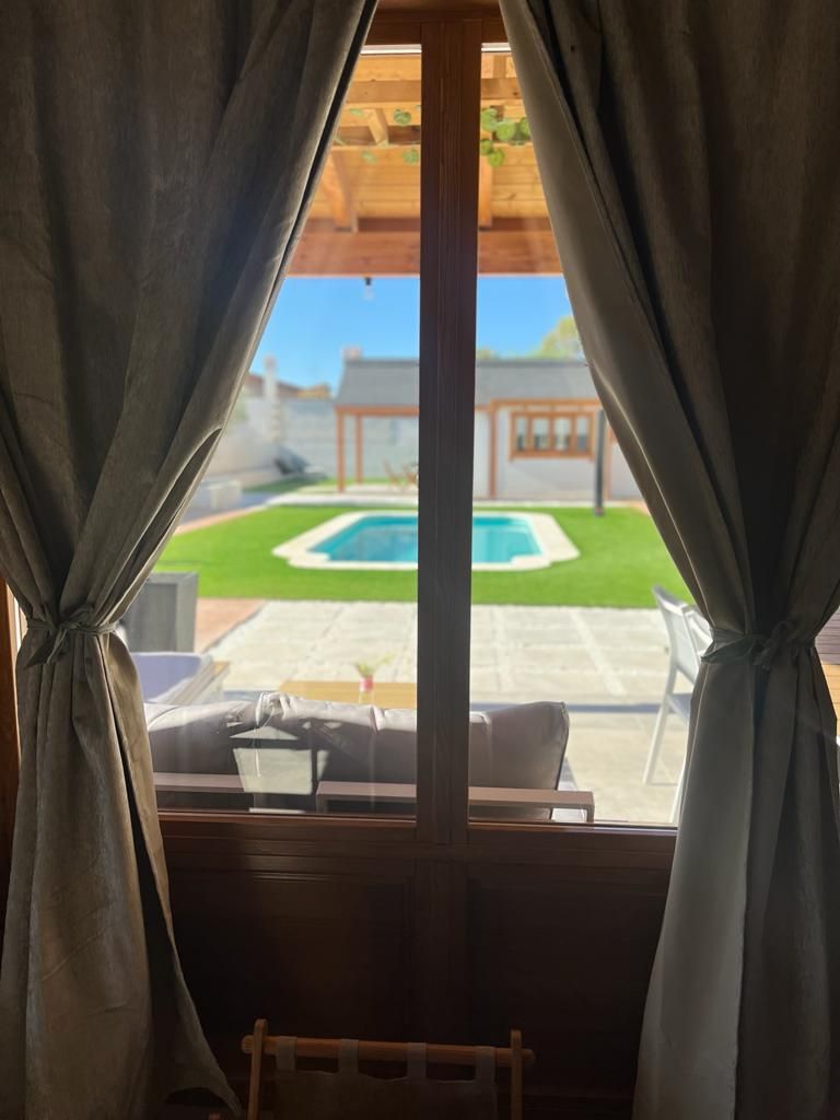 Una vista de una piscina a través de una ventana con cortinas.