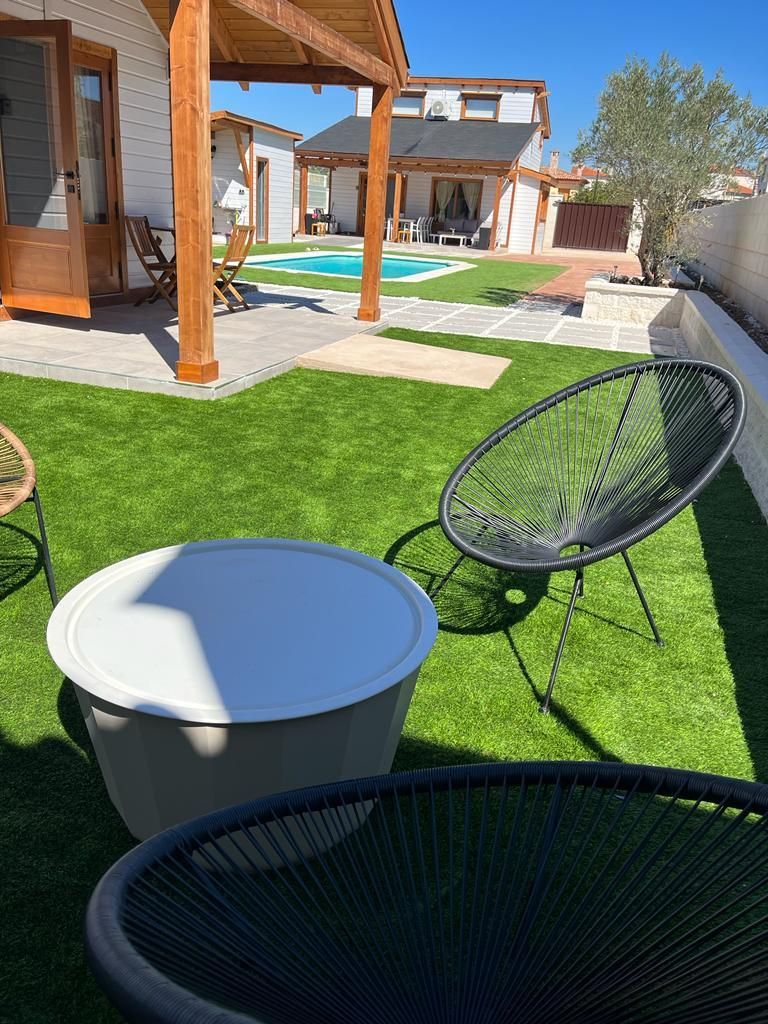 Un césped con una mesa y sillas delante de una casa con piscina.