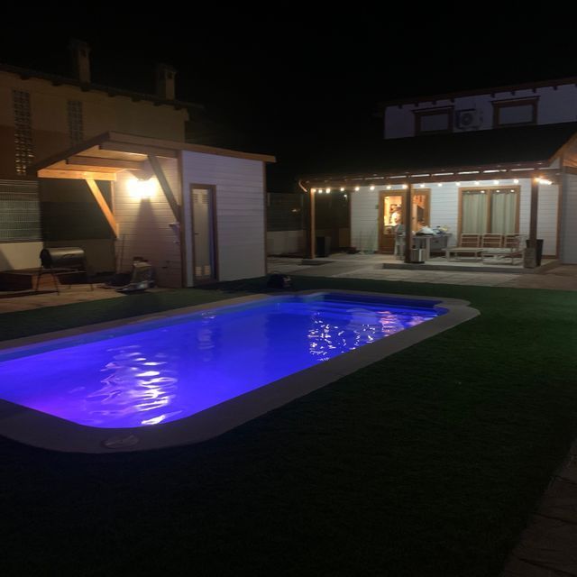 Una piscina está iluminada por la noche frente a una casa.