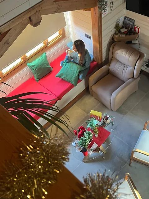 Una mujer se sienta en un sofá rojo leyendo un libro.
